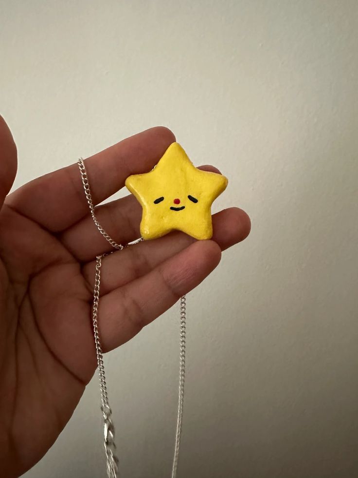 a hand holding a yellow star necklace with a face drawn on it's side