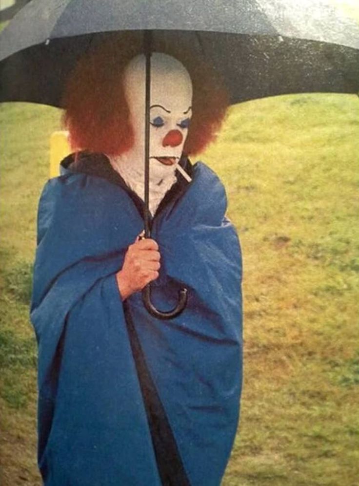 a clown holding an umbrella on the side of the road in the rain with it's head covered by a blue cloth