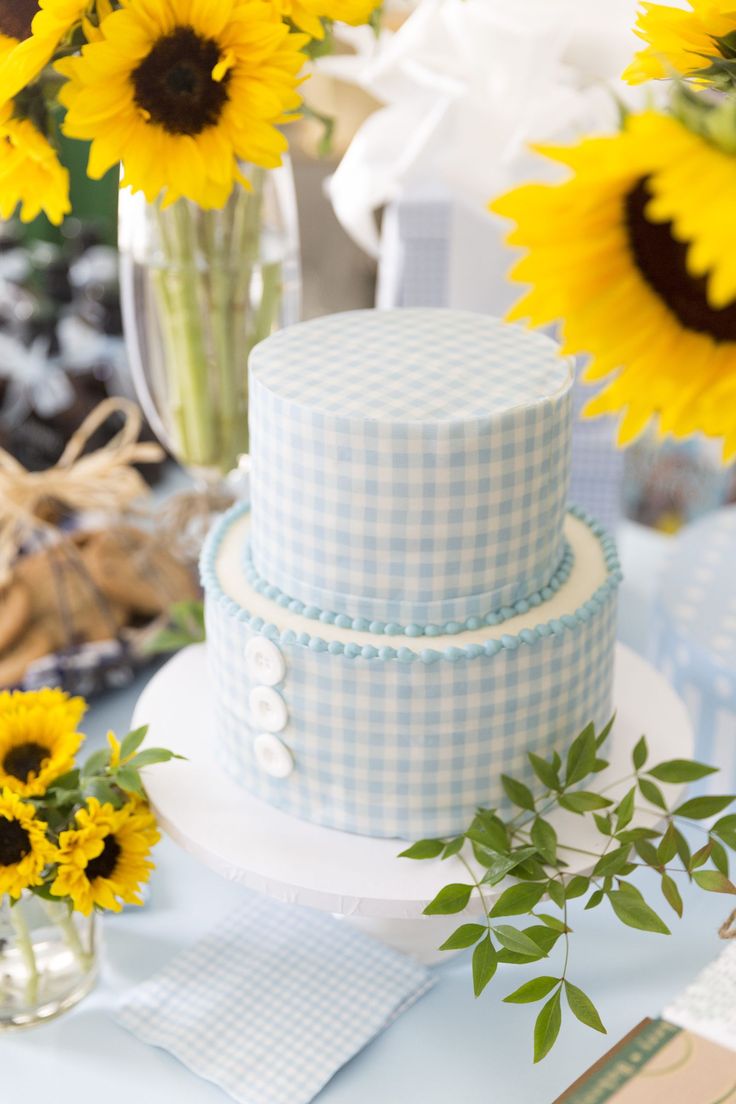 a blue and white cake sitting on top of a table next to sunflowers