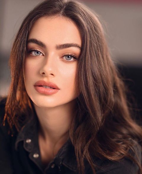 a woman with long brown hair and blue eyes is looking at the camera while wearing black shirt