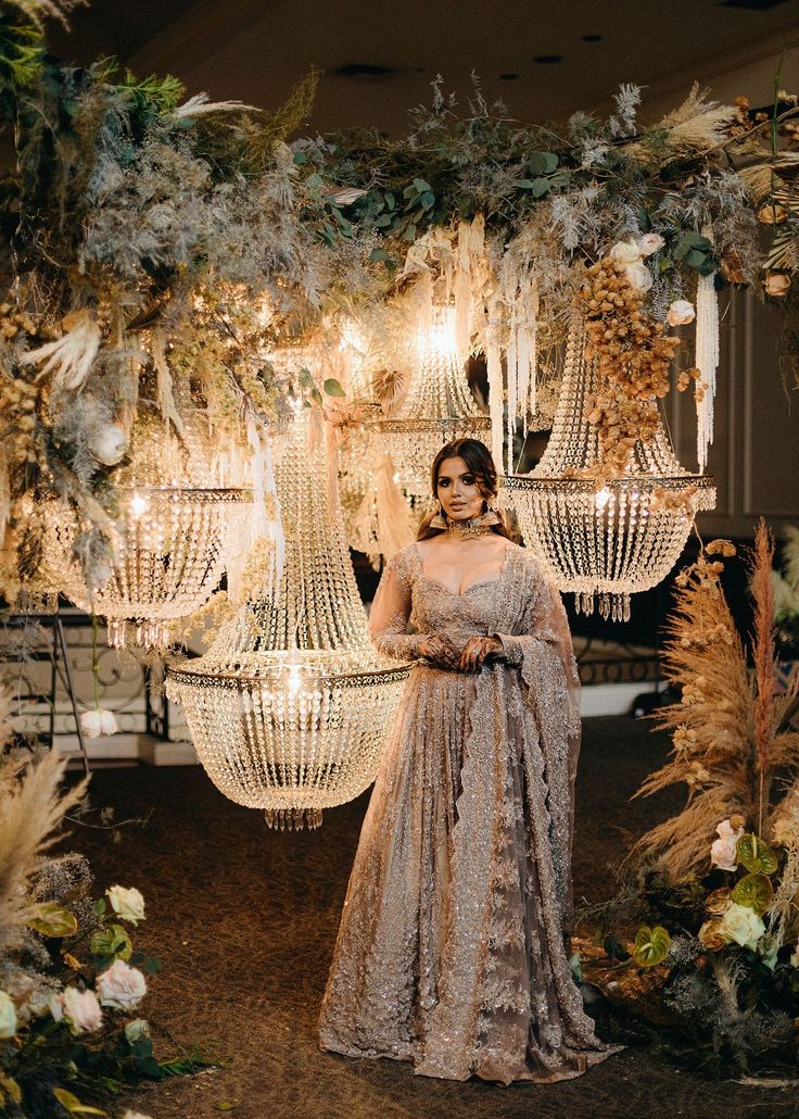 a woman standing in front of a chandelier with flowers and feathers on it