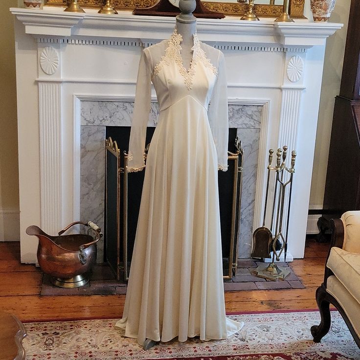 a white dress is on display in front of a fireplace with gold decorations and candles