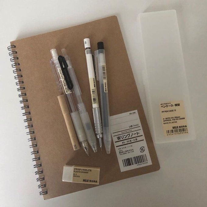 three pens and two erasers on top of a notebook