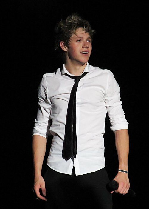 a male in a white shirt and black tie is singing into a microphone on stage