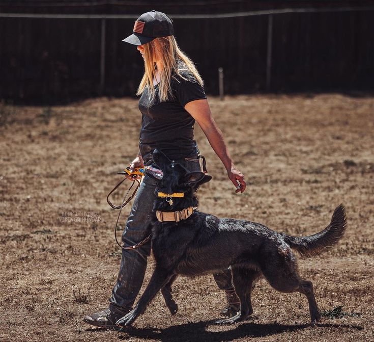 a woman is walking her dog on a leash in an open field with a fence behind her