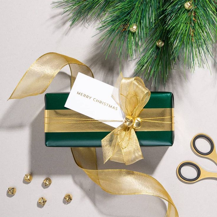 a christmas present wrapped in green and gold ribbon next to scissors, pine tree branch