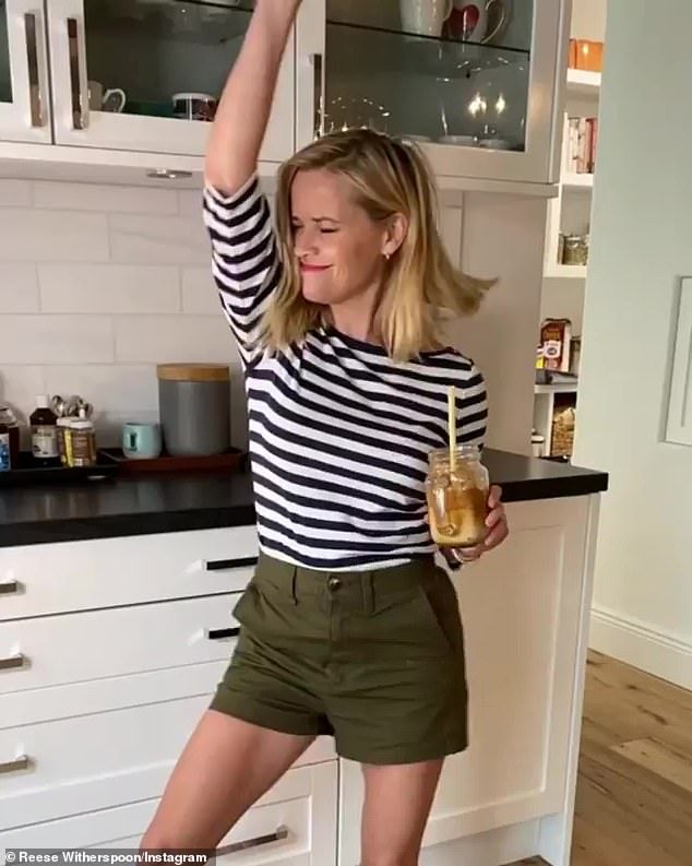 a woman standing in a kitchen holding a glass of beer and raising her arm up