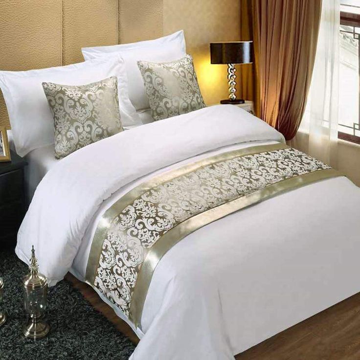 a bed with white and gold comforters in a bedroom next to a window,