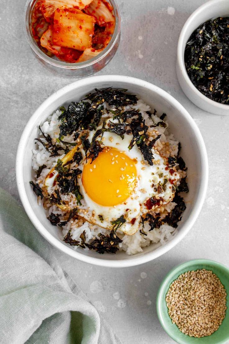 two bowls filled with rice, an egg and other ingredients on a white table cloth