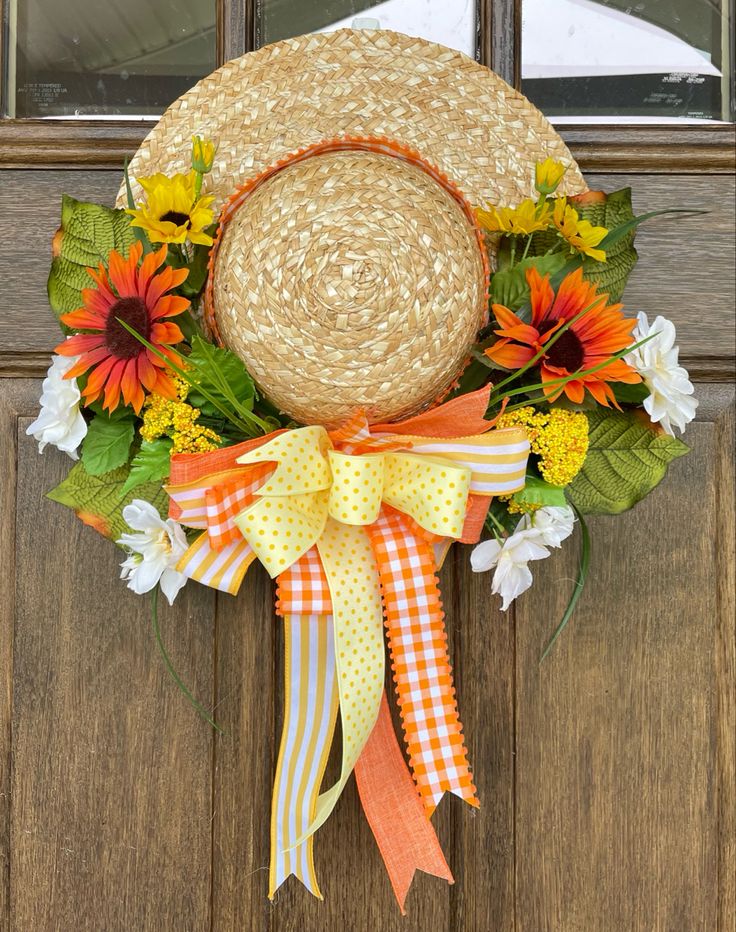 a straw hat is hanging on the front door with flowers and ribbons attached to it