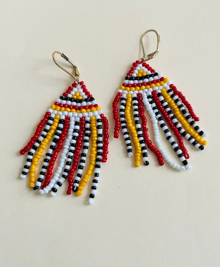 two pairs of colorful beaded earrings on a white surface with black, yellow and red beads