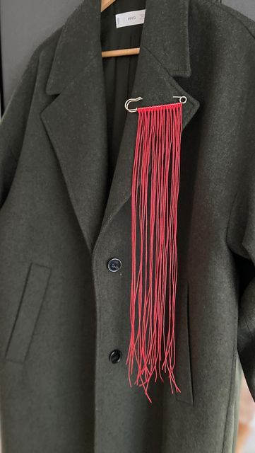 a gray coat with red fringes hanging from it's lapel on a hanger