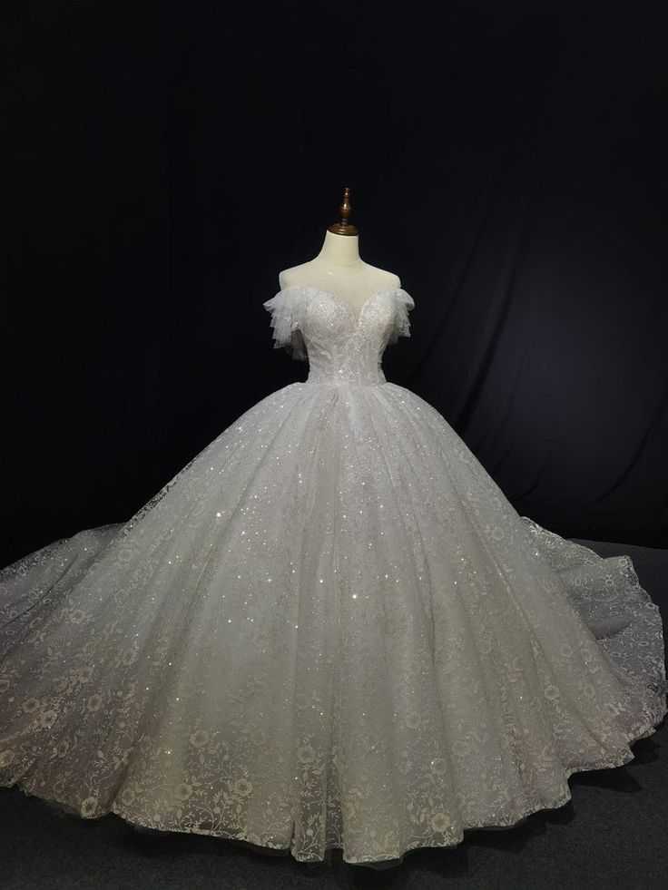 a white wedding dress on display in front of a black background with the back of it's gown covered in sequins