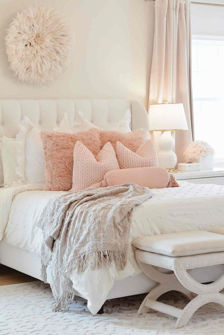 a white bed with pink pillows and blankets on it's headboard in a bedroom