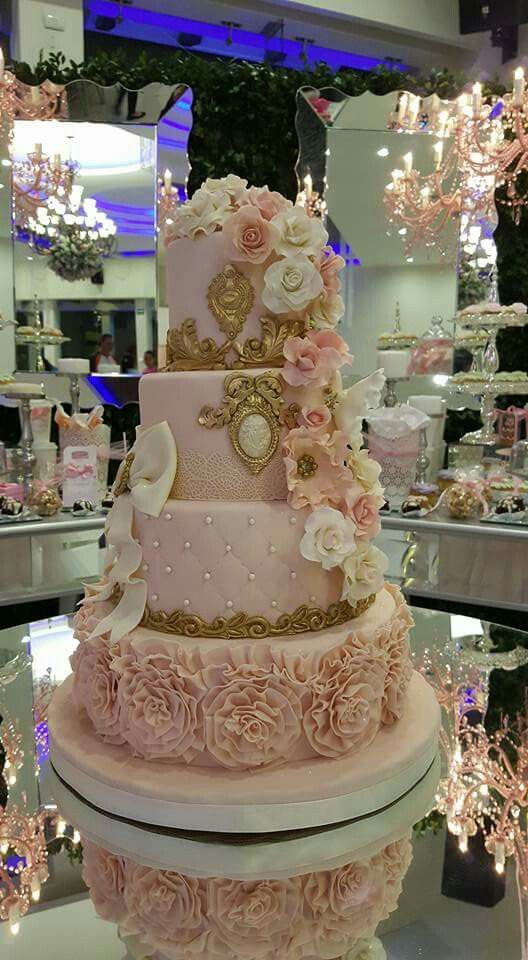 a pink and gold wedding cake with roses on it