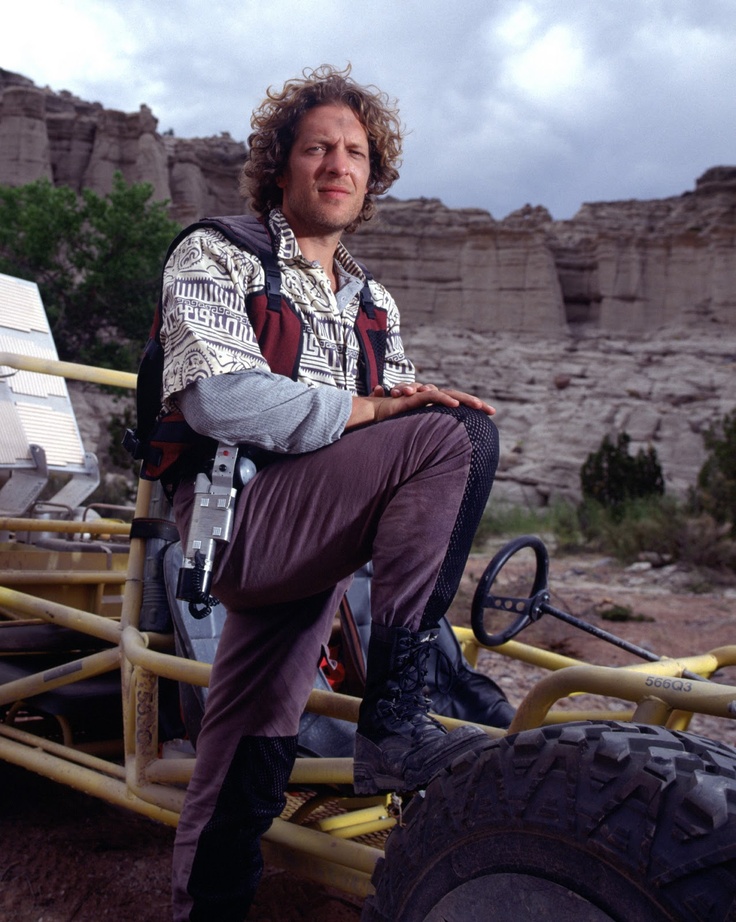 a man sitting on the back of a yellow vehicle in front of some rocks and trees