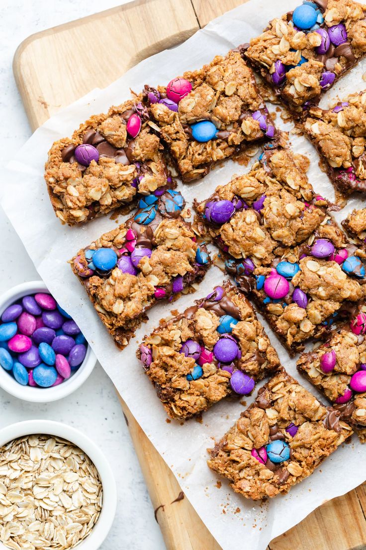 an assortment of cookies and candy bars on a cutting board next to bowls of oatmeal