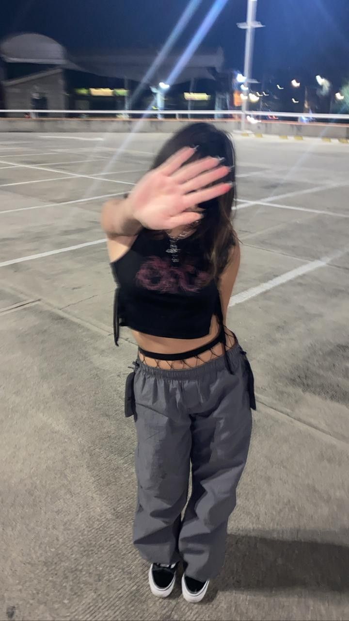 a woman standing in an empty parking lot with her hands up to her face and arms stretched out