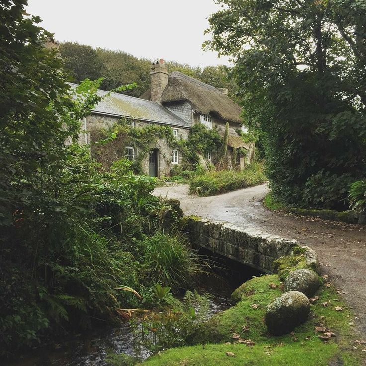 an old stone bridge crossing a small stream in front of a thatched roof house