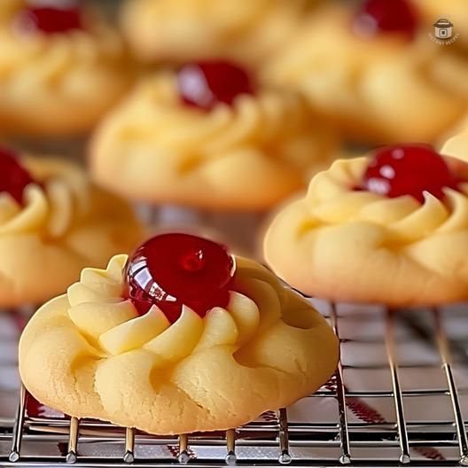 some cookies are cooling on a rack with cherries in the top, and one is topped with icing