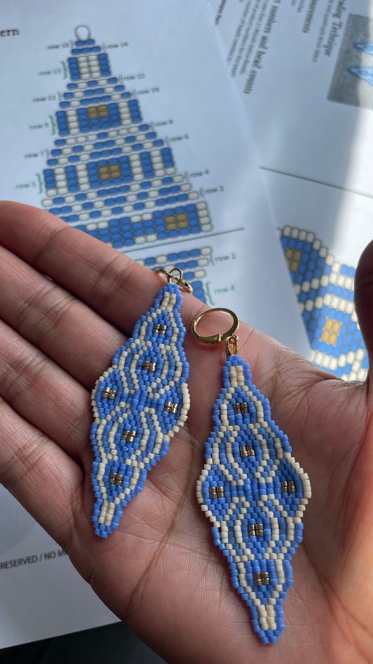 a person holding some kind of blue and white beaded earring in their hand