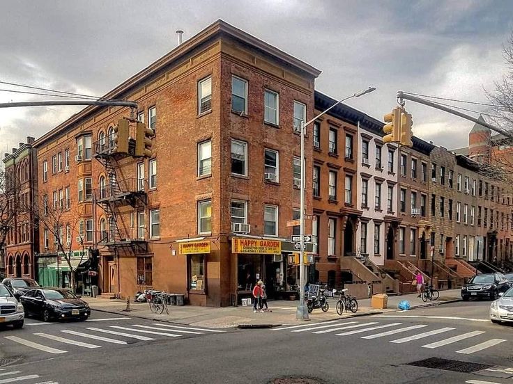 an intersection with cars, bicycles and people on the sidewalk in front of some buildings