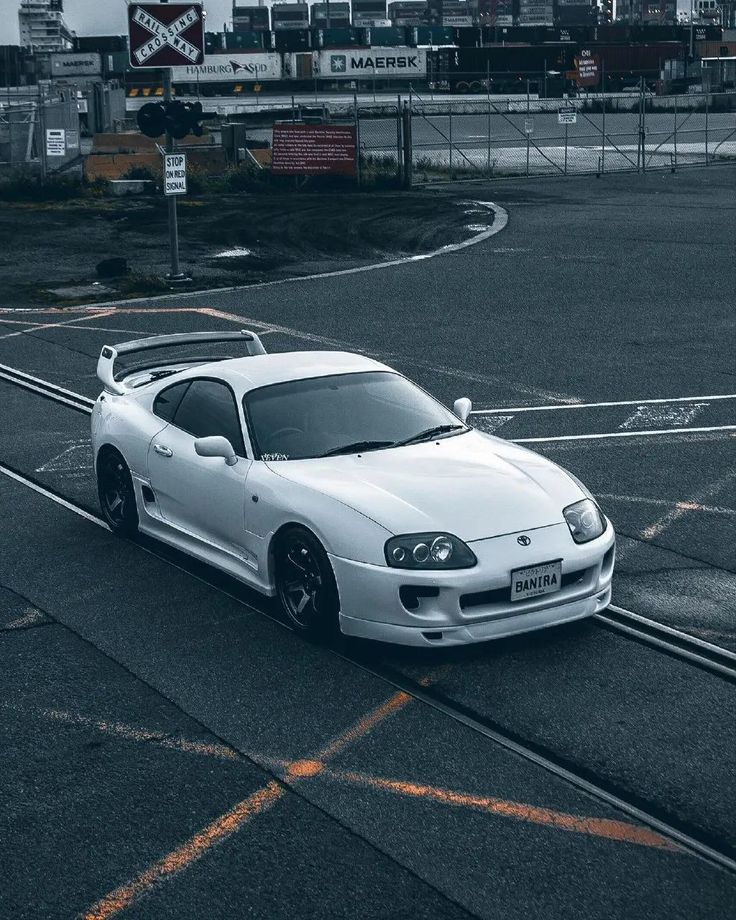 a white sports car is parked on the side of the road in an empty parking lot