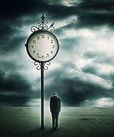 a man standing next to a tall clock on top of a dirt field under a cloudy sky