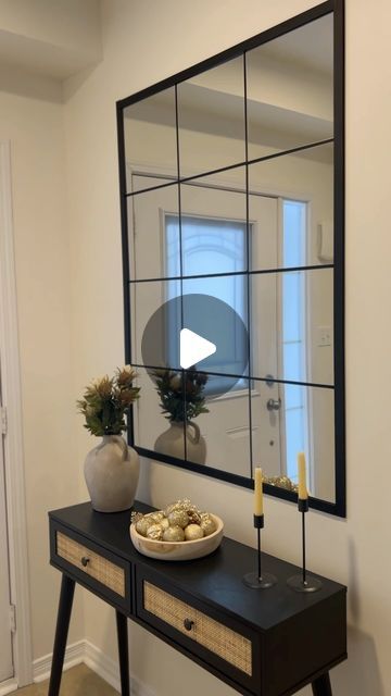 a mirror sitting on top of a wooden table next to a vase and candle holder