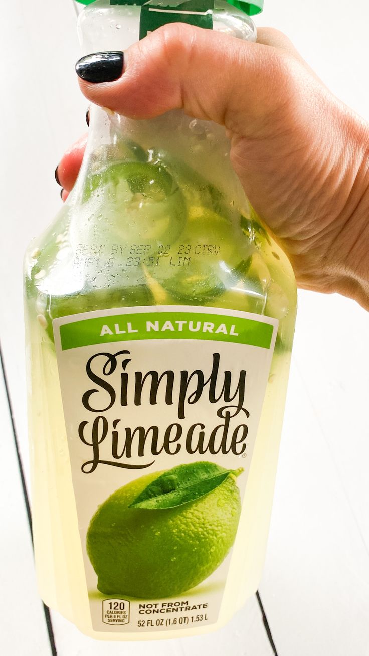 a hand holding a bottle of simply pineade with cucumber and lemon in it