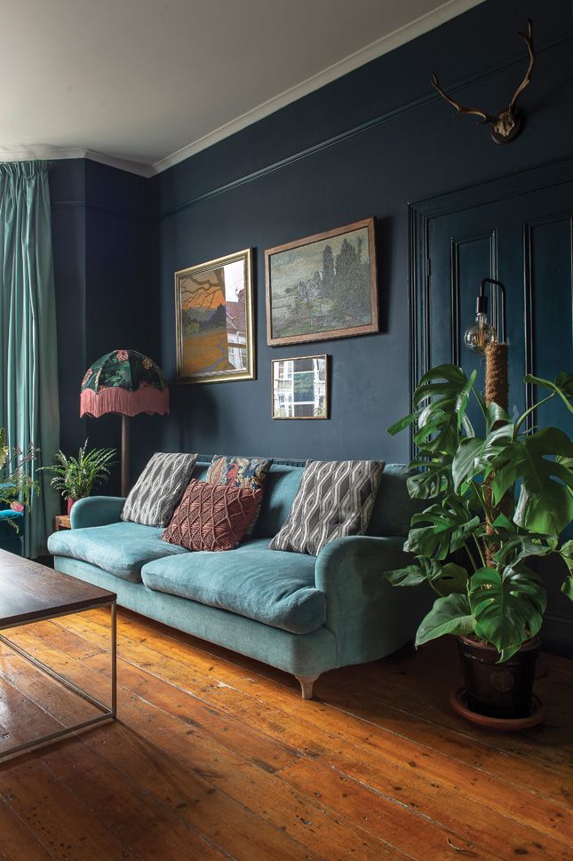 a living room with blue walls and wood flooring is pictured in this image, there are plants on the coffee table next to the couch