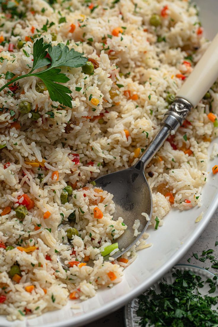 a white bowl filled with rice, carrots and parsley next to a spoon