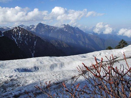 snow covered mountains and trees on a sunny day with clouds in the sky over them