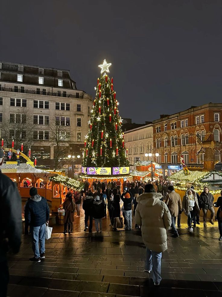 a large christmas tree is lit up in the middle of a crowded street at night