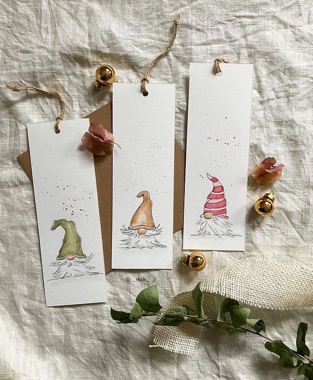 three bookmarks with gnomes on them sitting next to some flowers and bells,