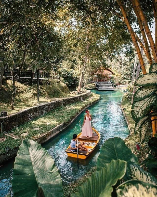 a man and woman in a small boat on a river surrounded by lush green trees