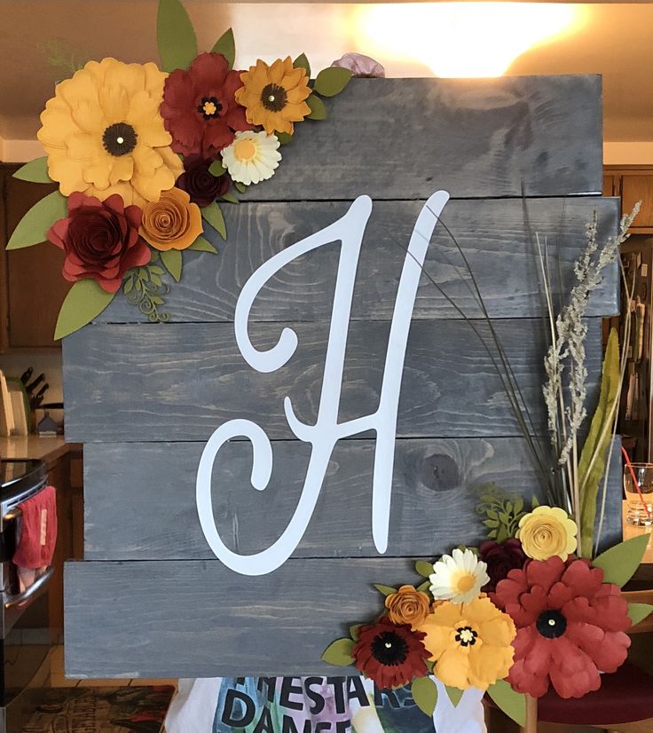 a wooden sign with flowers and the letter h painted on it's front side