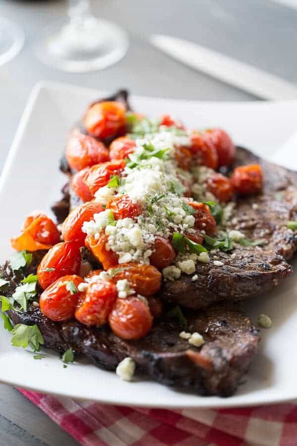 a white plate topped with steak covered in tomatoes and feta cheese on top of it