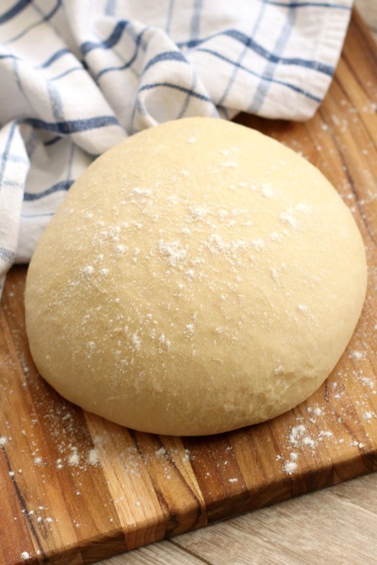 a ball of bread sitting on top of a wooden cutting board next to a blue and white towel