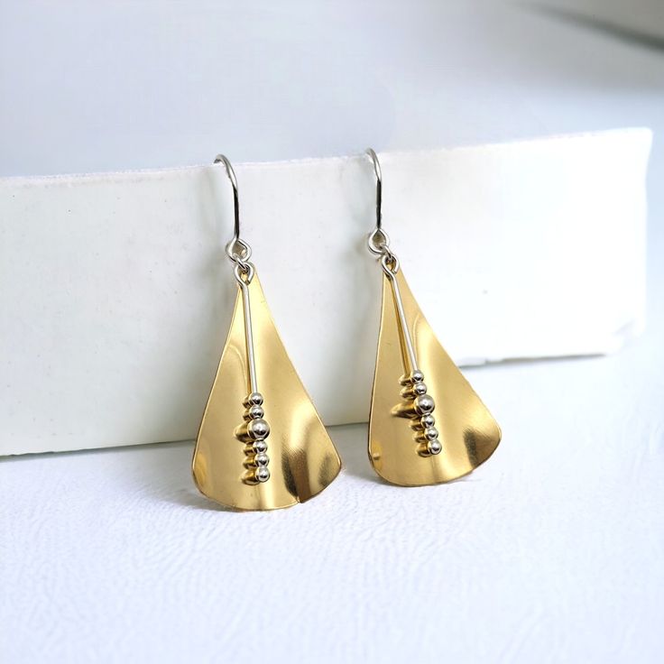 Embrace contemporary elegance with our Gold Geometric Triangle Dangle Earrings. Crafted with luxurious gold brass and sterling silver, these unique earrings feature a sleek triangle design that adds a touch of modern sophistication to any outfit. Make a statement with these exclusive earrings that exude luxury and style. Sterling Silver & Brass Approximately 2" long Polished to a High Shine Sent in a Ribboned Gift Box with Polishing Cloth Made in Montana Everyday Gold Triangle Earrings, Triangle Gold Earrings, Handmade Gold Triangle Jewelry, Gold Triangle Earring, Exclusive Earrings, Gold Triangle Metal Earrings, Luxe Necklace, Threader Earrings Gold, Silver Threader Earrings