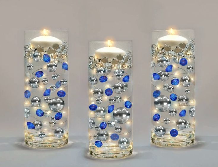 three clear glass vases with blue and silver balls on them, one has a lit candle in the middle