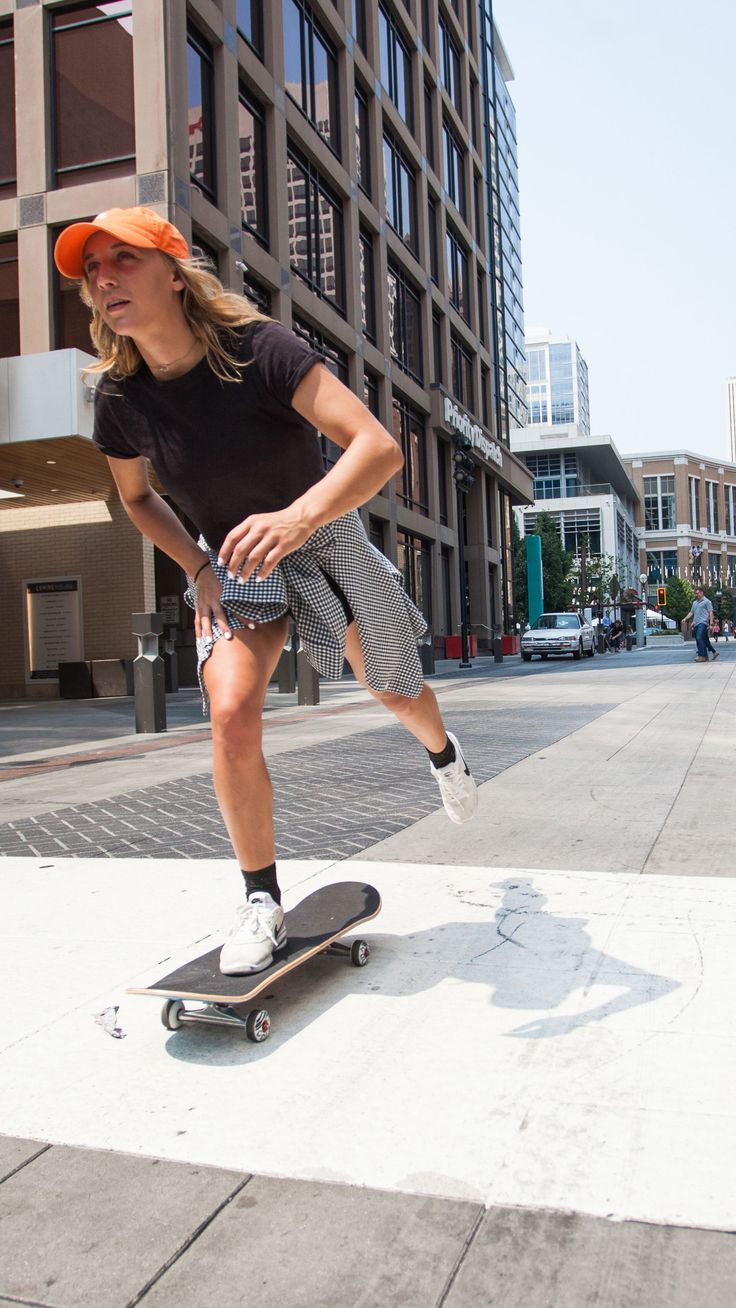 a woman riding a skateboard down the side of a sidewalk next to tall buildings