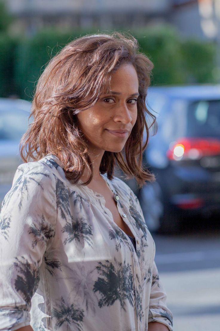 a woman standing on the street with her hands in her pockets and looking at the camera