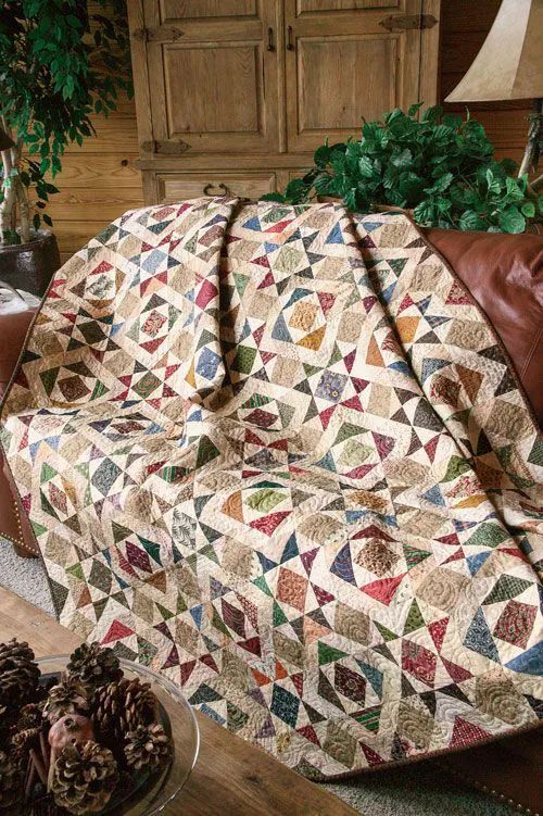 a couch covered in a quilt next to a table with two pine cones on it