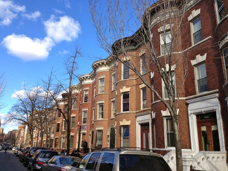 several cars parked on the street in front of some brick buildings with windows and balconies