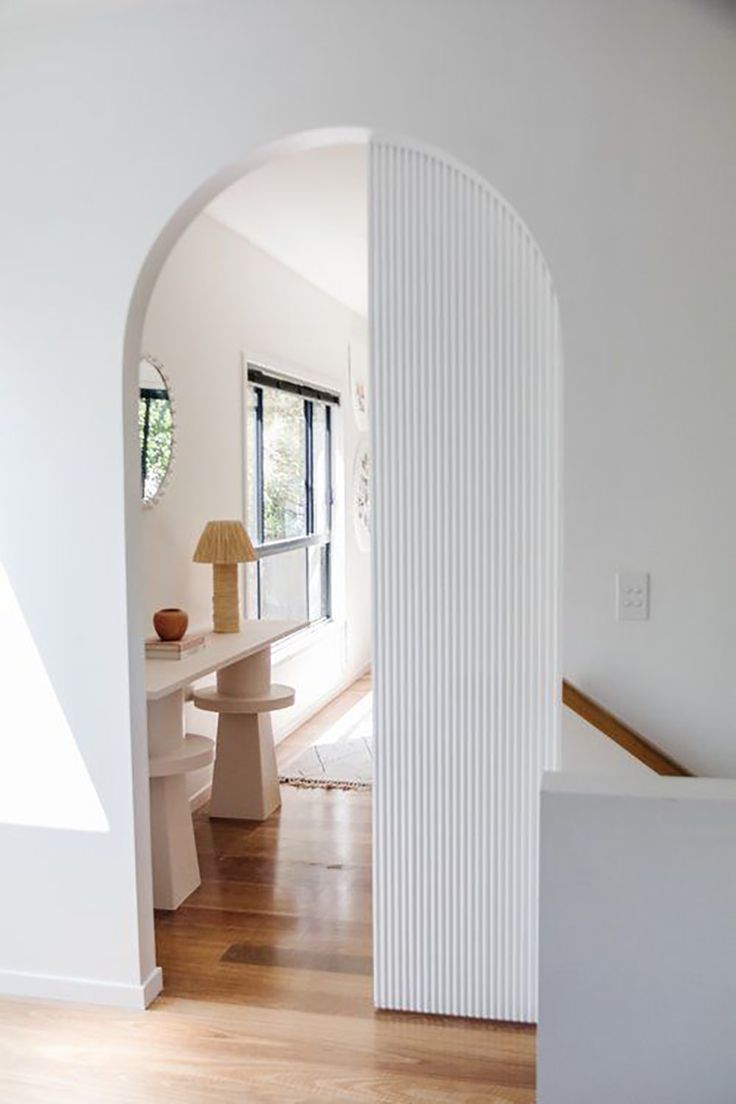 an archway leading into a living room with white walls and wood floors, along with a lamp on the end table