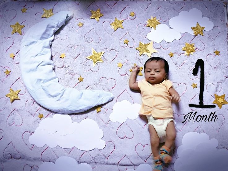 a baby laying on top of a bed next to a moon and stars wallpaper