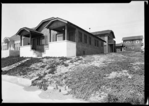 black and white photograph of two houses on top of a hill with grass growing in the foreground