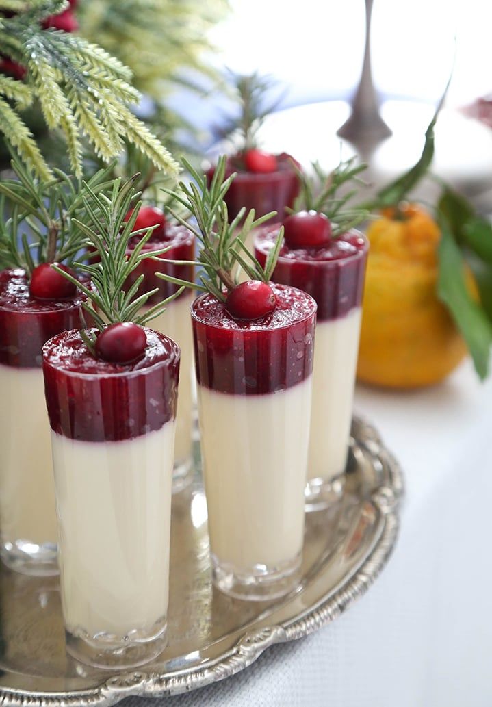 four glasses filled with cranberry jello sitting on a silver tray next to pine branches