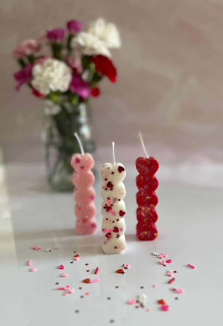 three candles are sitting next to each other on a table with flowers in the background